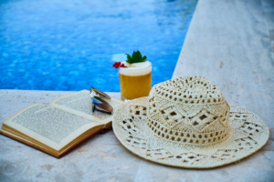 View of a poolside with a hat, drink, book and sunglasses placed